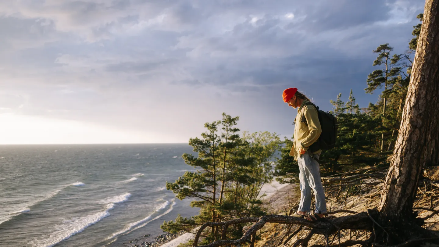 Man som står på en trädrot vid landborgkanten med utsikt över Kalmarsund.